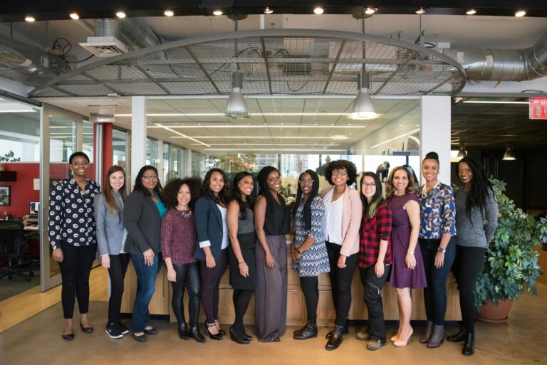 A diverse group of women in technology poses together in an office lobby, exuding confidence and teamwork.