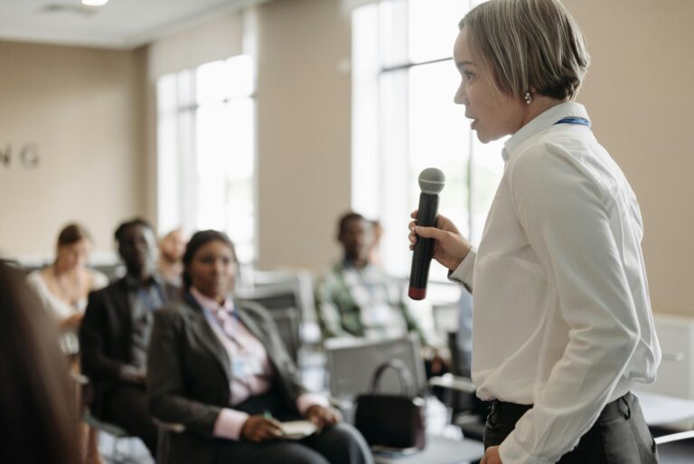 Side view of a businesswoman holding a microphone while addressing an audience at a conference.